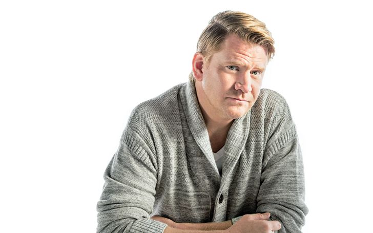 A man in his forties wearing a grey cardigan.