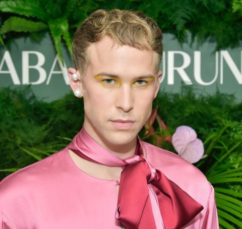 Tommy Dorfman in a pink outfit poses during a photoshoot.