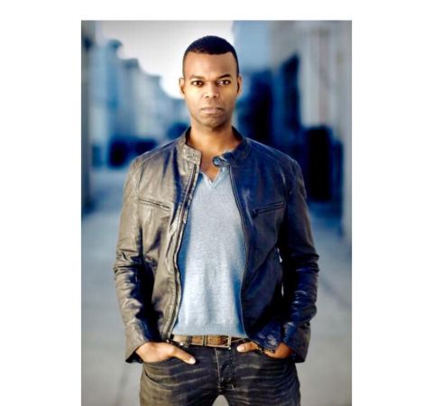 Demore Barnes in a black jacket and black pant poses during a photoshoot.