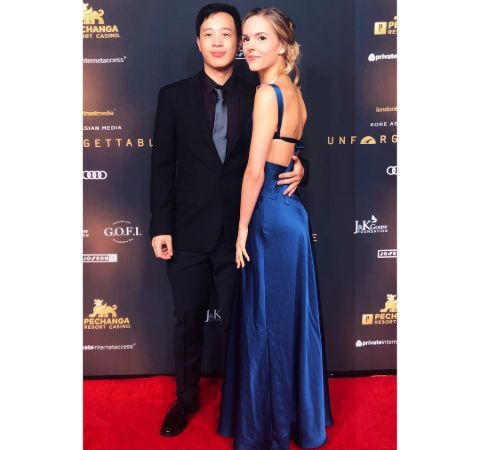 Kari Perdue in a blue dress poses alongside actor Hayden Szeto at an event.