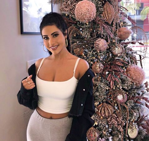 Yasmin Kavari in a white  top and pant poses in front of a Christmas tree.