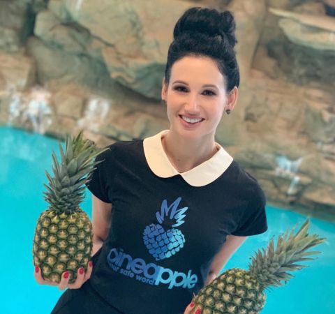 Amie Harwick In a black t-shirt holding pineapples in her hands.