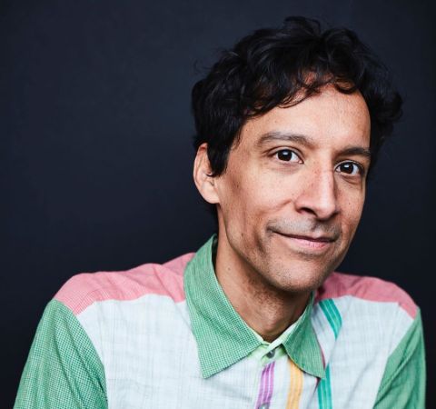 Comedian Danny Pudi in a green t-shirt poses for a picture.