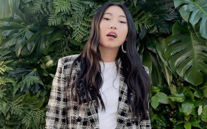Awkwafina posing for a picture in a white t shirt and a checked outer